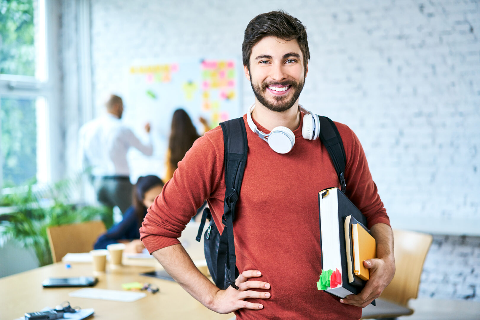 Portrait of male student standing with books in classroom and looking at camera