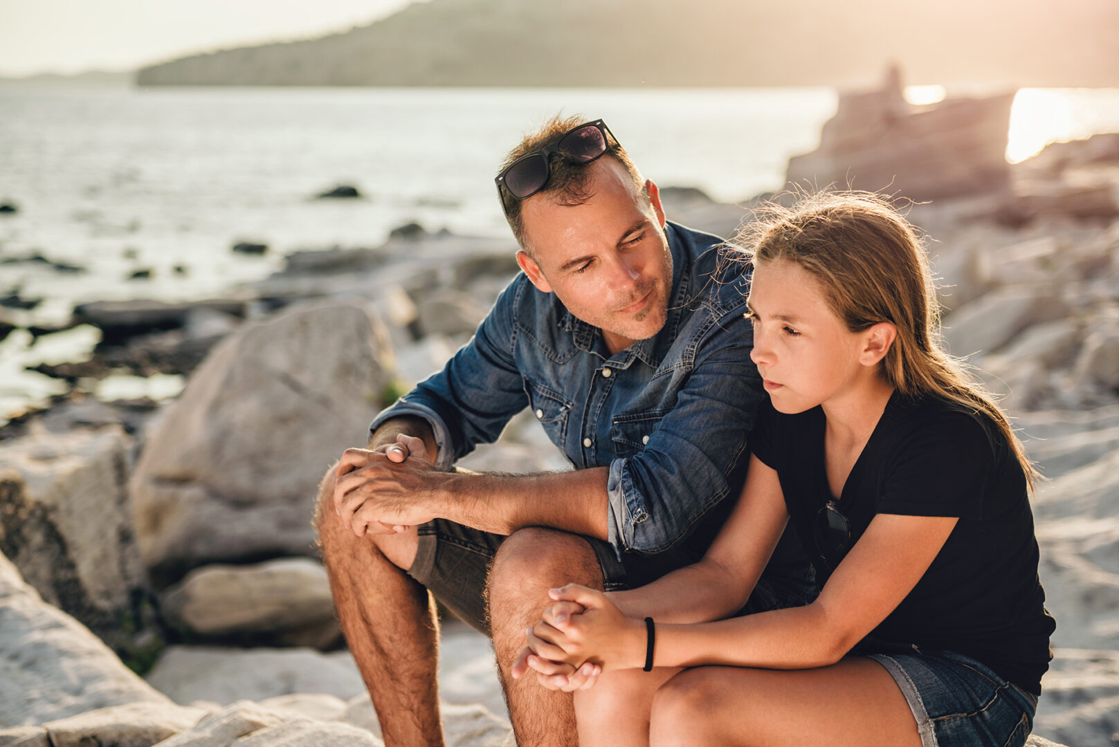 Father and daughter relaxing on a rocky beach by the sea and having time together