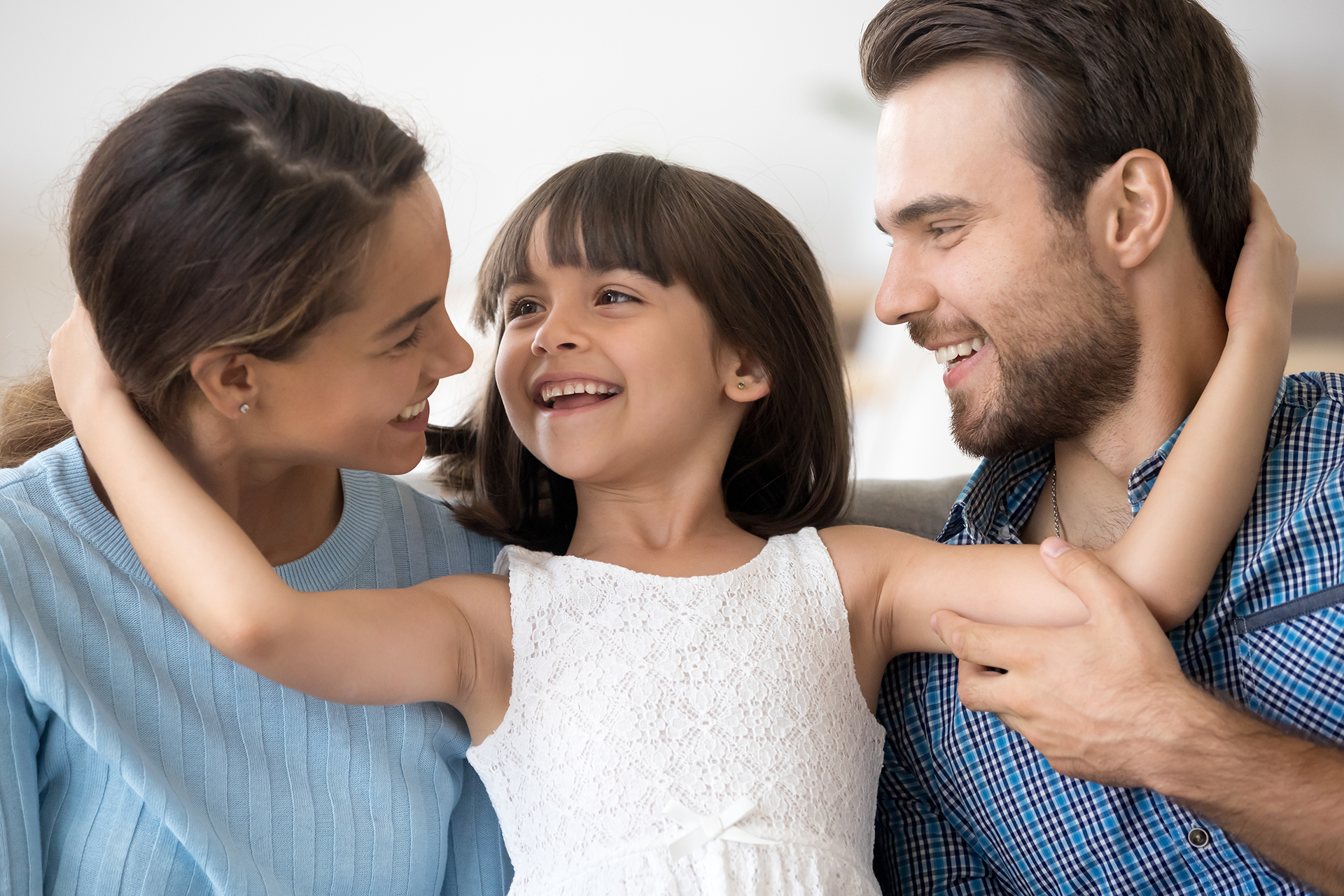 Portrait of multi-ethnic attractive mother father adorable little preschool daughter sitting together looking at each other embracing. New parents for adopted child or happy wellbeing family concept