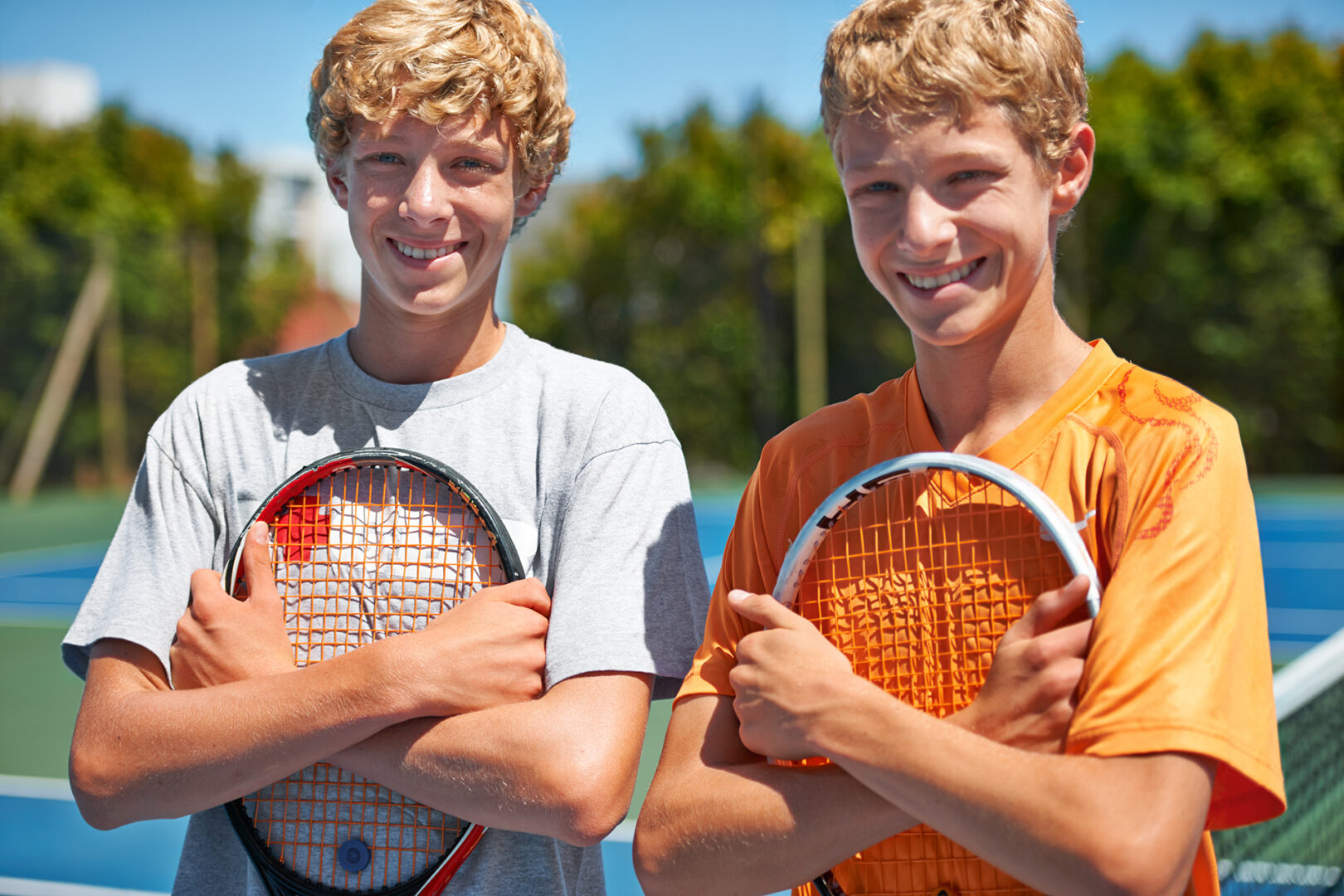 Two friends standing together and holding their tennis rackets on the court