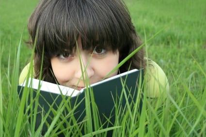 Pretty girl on the grass looking over the book